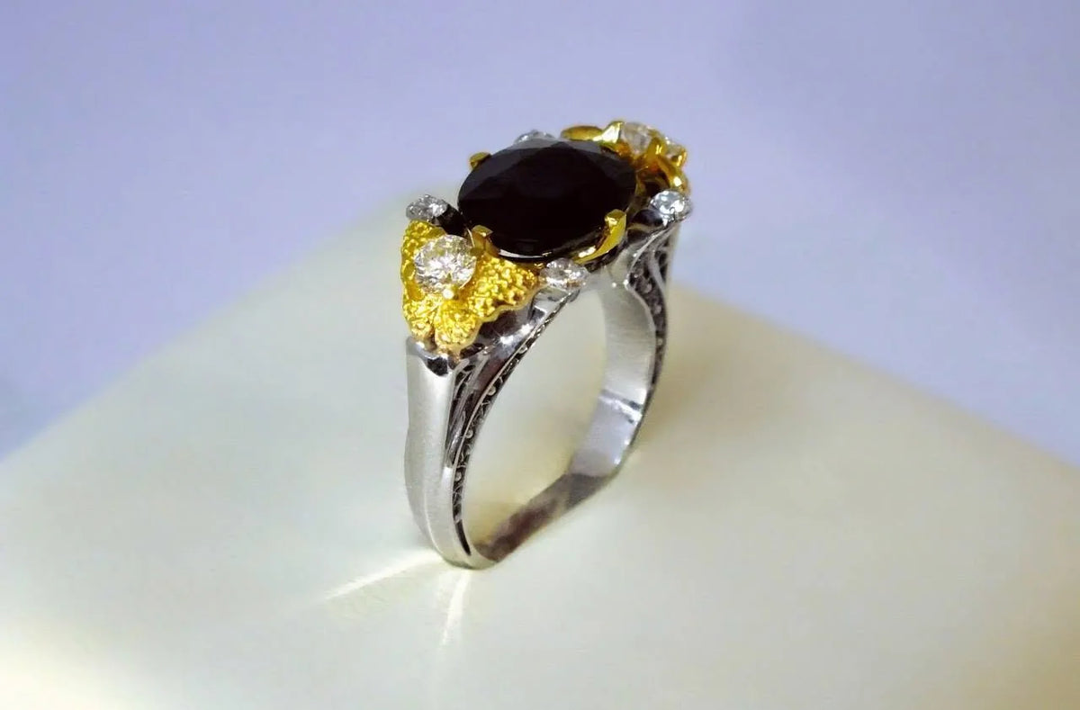 Safirring i hvidguld og gult guld set skråt fra siden med diamanter og gulddetaljer